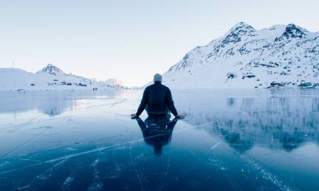 man-sitting-on-a-frozen-lake-looking-at-mountains