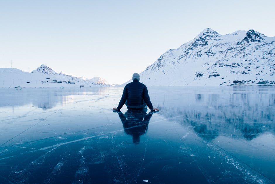 man-sitting-on-a-frozen-lake-looking-at-mountains